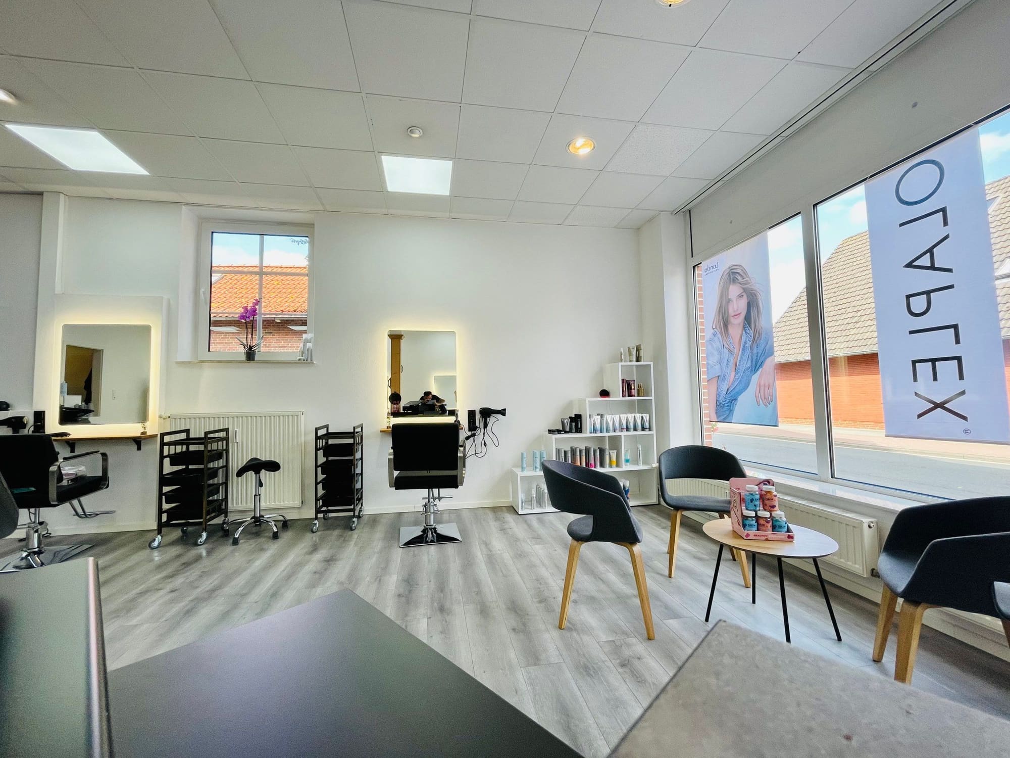 Der Salon von innen: heller Raum, Holzstützen, schwarze Stühle, große Fenster zur Straße
